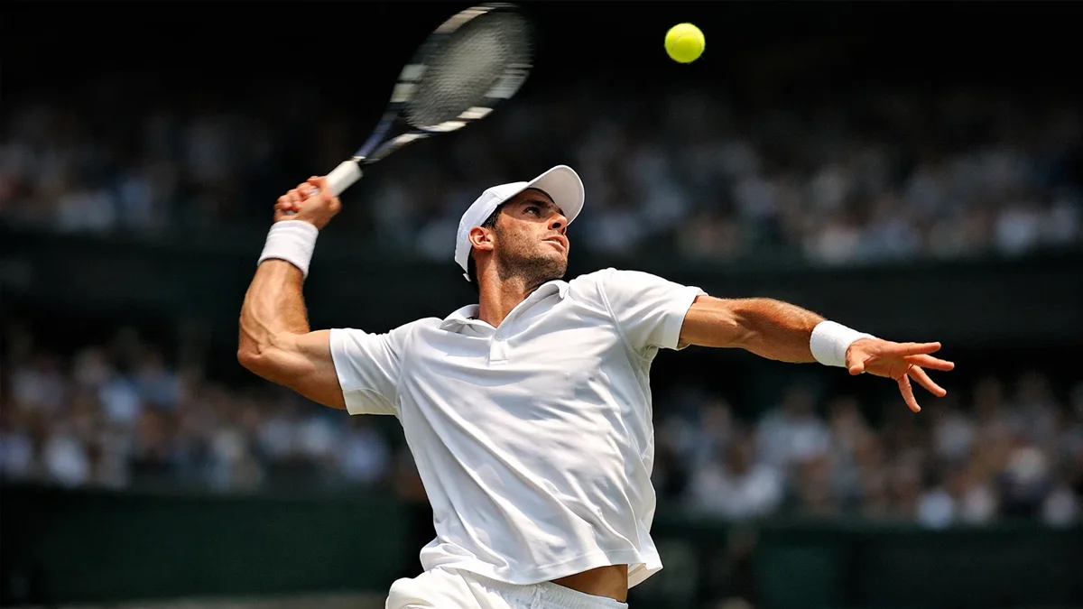 Tennisspieler in weißer Wimbledon-Kleidung beim kraftvollen Aufschlag auf dem Rasenplatz